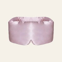 Masque de sommeil en soie rose poudré, présenté de face sur fond clair.