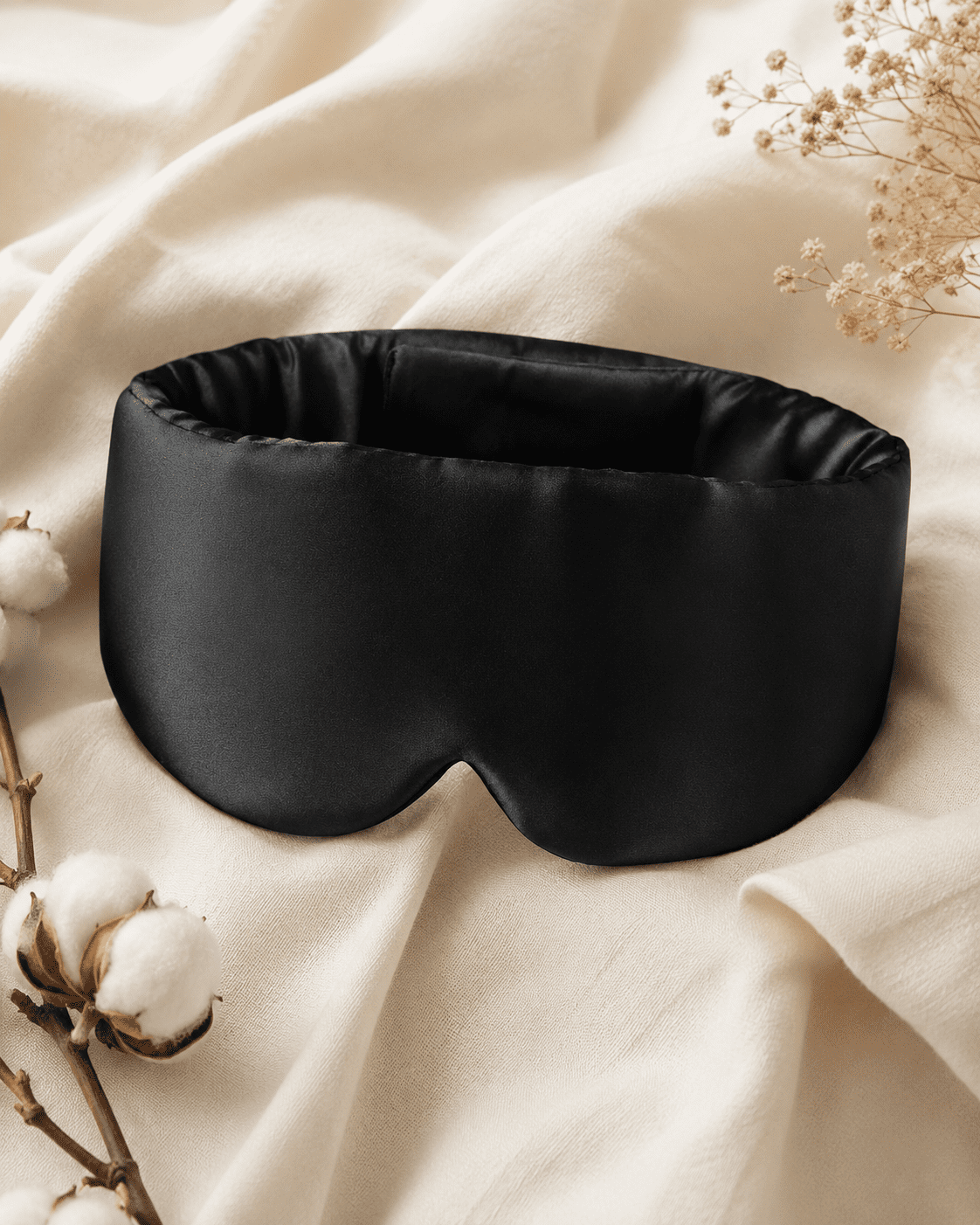 Masque de sommeil en soie noir posé sur un tissu clair. Image